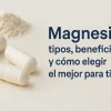 Cápsulas blancas de suplemento sobre fondo beige con polvo de magnesio y texto “Magnesio: tipos, beneficios y cómo elegir el mejor para ti